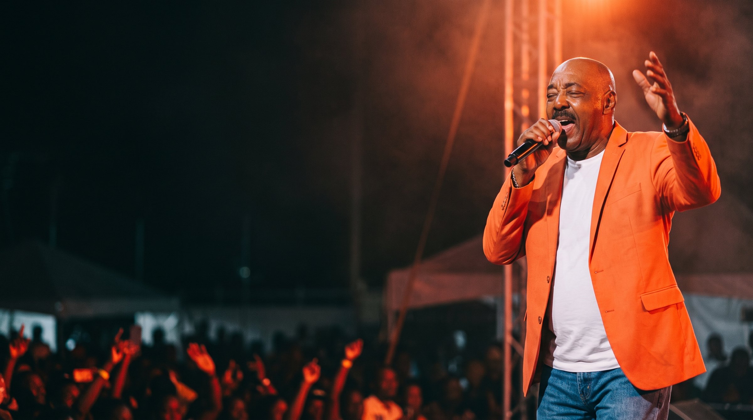 DMANLYRICS performing on stage in his orange jacket, mic in hand